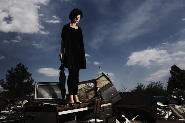 woman on top of discarded junk, holding and umbrella
